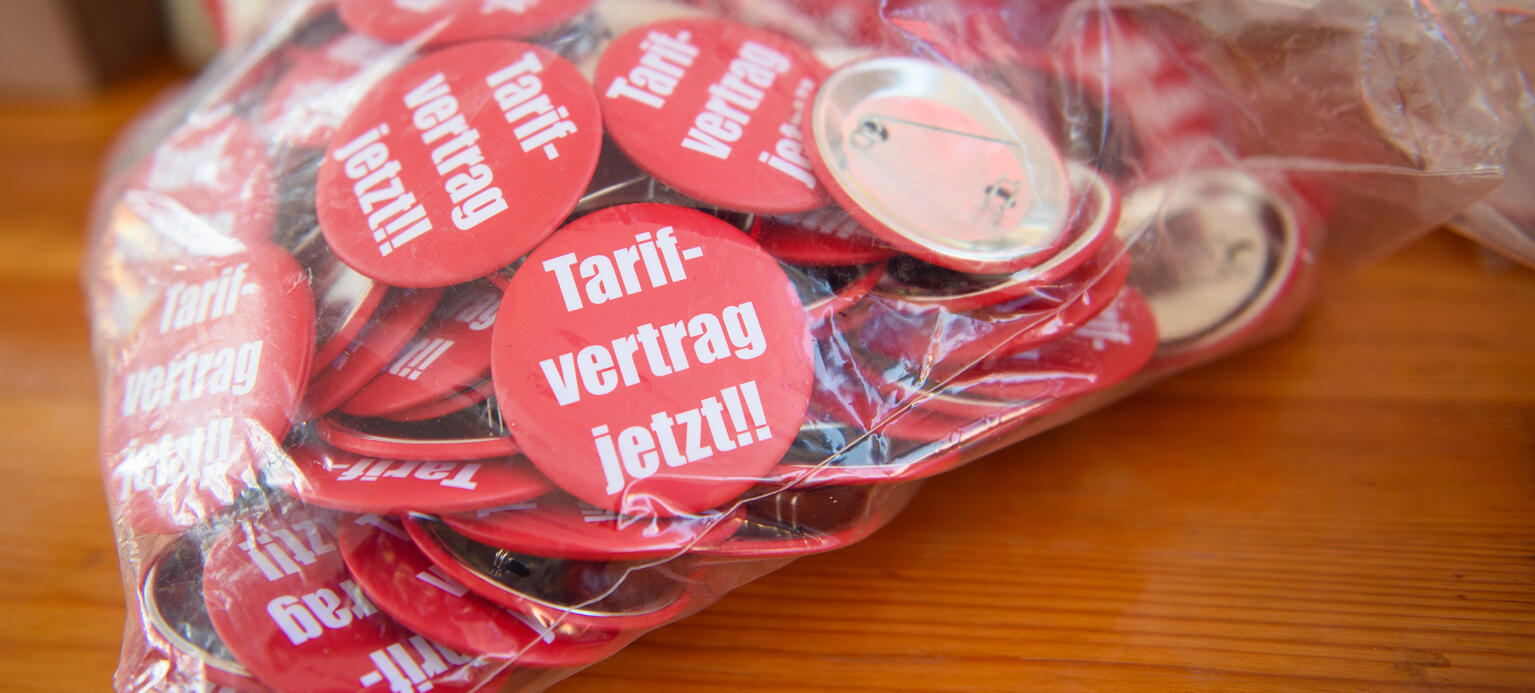 Buttons mit der Aufschrit „Tarifvertrag jetzt!!“ der Gewerkschaft IG BAU liegen in einer Plastiktüte auf einem Tisch. PM Tarifautonomie