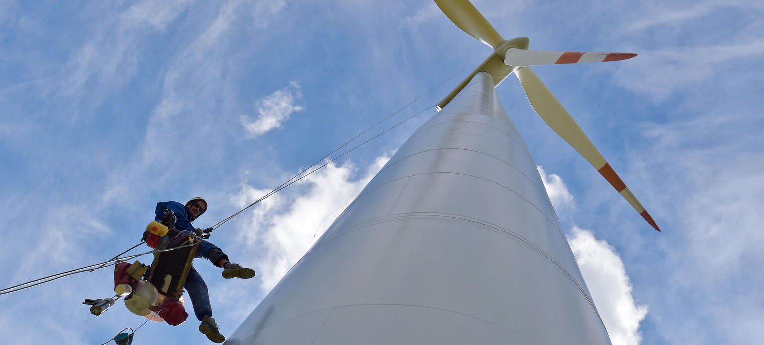 Ein Industriekletterer hängt in luftiger Höhe an dem Mast einer Windenergieanlage 