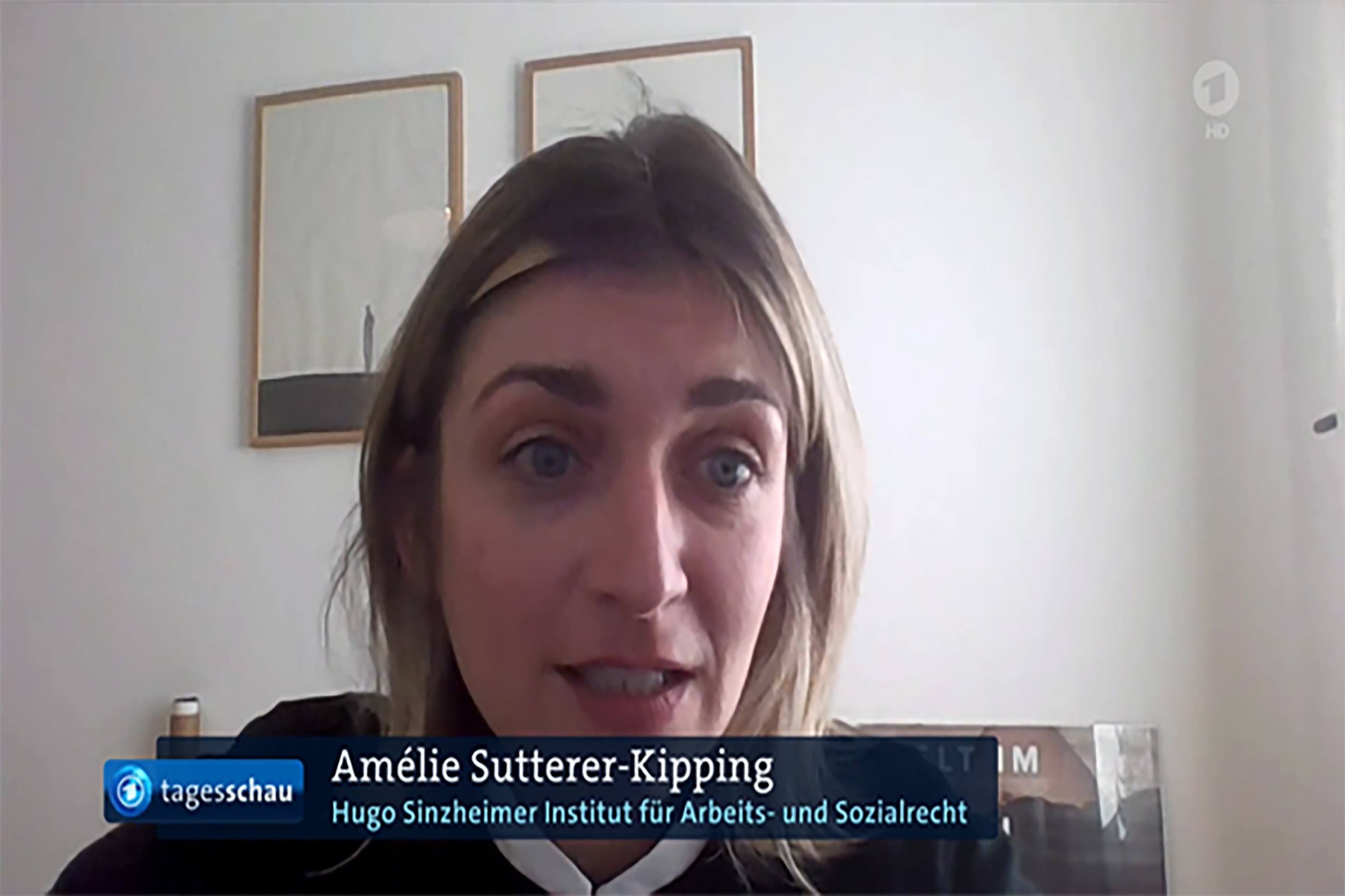 Amélie Sutterer-Kipping während ihres Statements bei der tagesschau. Sie sitzt vor einer weißen Wand mit zwei Bildern.